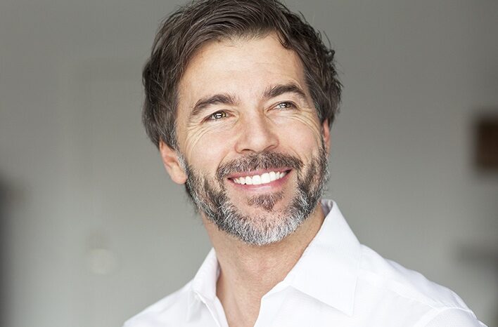 Photograph of a middle-aged man with a black and white beard and short black hair smiling and looking off into the distance.